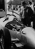 1936, Ferdinand Porsche betrachtet den 16-Zylinder-Kompressor-Motor im Auto-Union-Rennwagen (Porsche Typ 22). Es galt die 750 Kilogramm-Formel, die das Gewicht des Rennwagens auf 750 Kilogramm beschränkte.